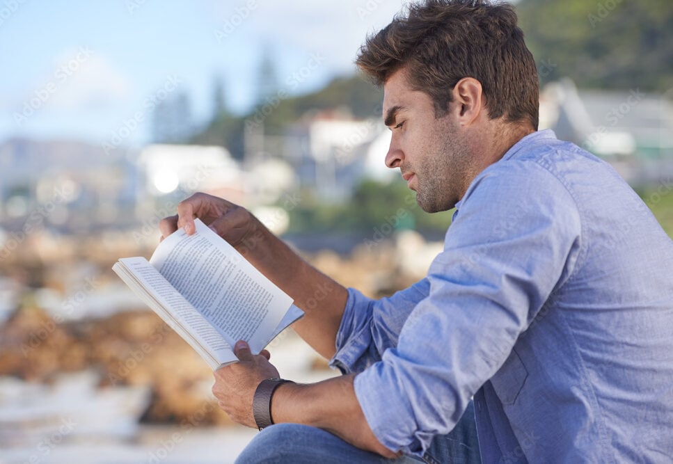 Novels are a great way to relax. A young man reading a book outdoors. 100 books every person should read.